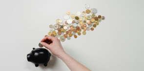 A pile of coins and a hand putting a coin into a piggy bank